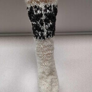 K&ouml;nnte beinhalten: Wei&szlig;e Stricksocken mit einem schwarz-wei&szlig;en geometrischen Muster am oberen Teil der Socke.