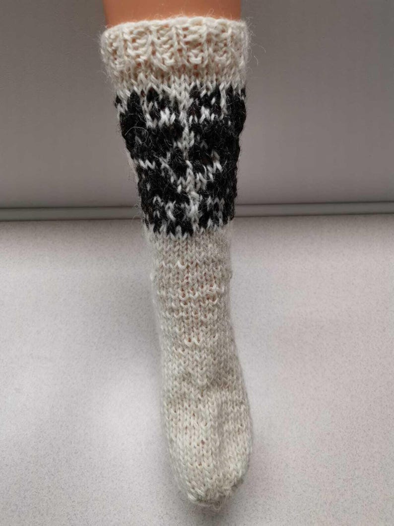 K&ouml;nnte beinhalten: Wei&szlig;e Stricksocken mit einem schwarz-wei&szlig;en geometrischen Muster am oberen Teil der Socke.