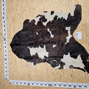 Könnte beinhalten: Schwarz-weißer Kuhfellteppich mit braunem und weißem Muster. Der Teppich ist etwa 190 cm breit und 160 cm lang.