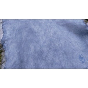 May include: A close-up of a light blue suede fabric with a subtle marbled pattern. The fabric has a soft, velvety texture.