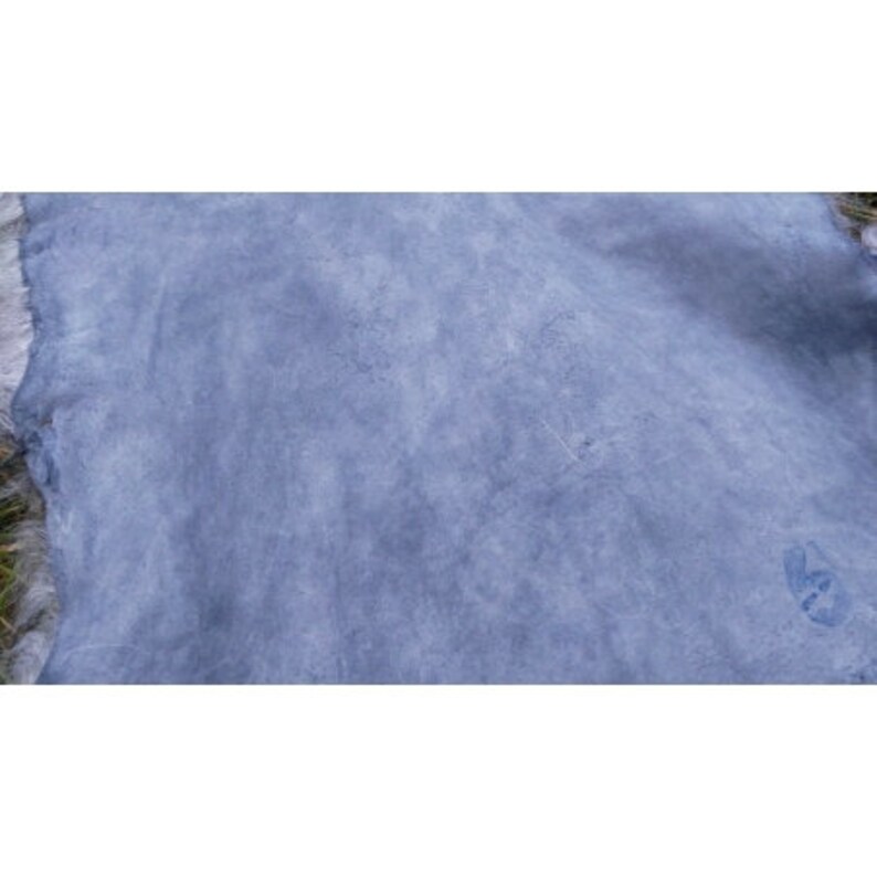 May include: A close-up of a light blue suede fabric with a subtle marbled pattern. The fabric has a soft, velvety texture.
