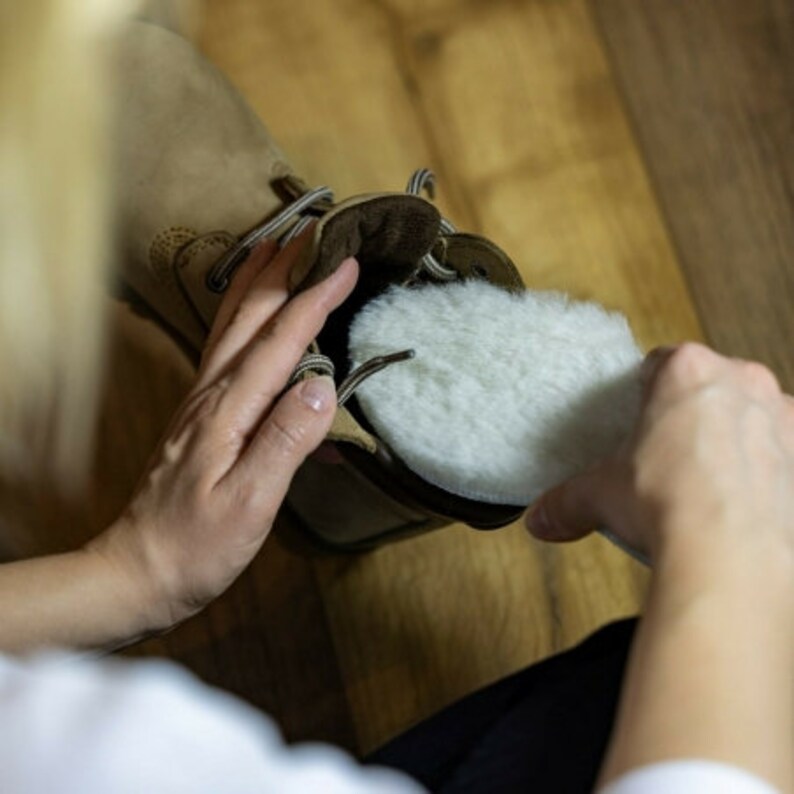 Peut inclure: Une personne ins&egrave;re une semelle int&eacute;rieure en peau de mouton blanche dans une botte en cuir marron. La semelle int&eacute;rieure est ronde et moelleuse.