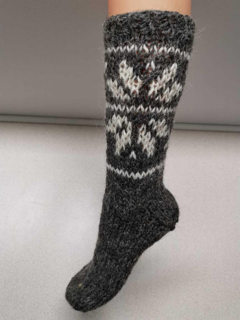 K&ouml;nnte beinhalten: Graue Wollsocken mit einem wei&szlig;en Schneeflockenmuster. Die Socken sind gestrickt und haben eine flauschige Textur.