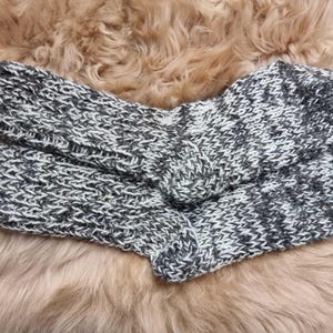 K&ouml;nnte beinhalten: Ein Paar kuschelige, gestrickte Socken in einem grau-wei&szlig;en Farbschema. Die Socken sind aus einem weichen, flauschigen Garn gefertigt und haben ein strukturiertes Strickmuster.