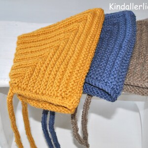 Pode incluir: Três gorros de bebê de malha em amarelo mostarda, azul e marrom, com laços. Os gorros são exibidos em uma superfície branca. O texto "Kindallerliebst" é visível no canto superior direito.