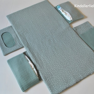 May include: A green changing mat with white polka dots and multiple pockets. The pockets are made of a waffle-like fabric. The mat is folded in half and has the text "Kindallerliebst" printed on it.