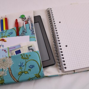 Könnte beinhalten: Ein Notizbuchcover aus blau-weißem Stoff mit Taschen für Stifte, Bleistifte und andere Kleinigkeiten. Das Cover ist an einem spiralgebundenen Notizbuch mit weißem kariertes Papier befestigt.