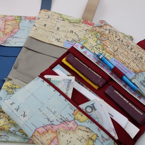 Könnte beinhalten: Drei Reisegeldbörsen mit Weltkarten-Design. Die Geldbörsen sind in verschiedenen Farben: blau, grau und rot. Jede Geldbörse hat mehrere Fächer und einen Reißverschluss. Die Geldbörsen sind gefüllt mit Bargeld, Karten und einem Stift.