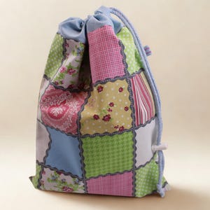 Könnte beinhalten: Ein Patchwork-Beutel mit Kordelzug und einer Vielzahl von gemusterten Quadraten in Rosa, Grün, Blau und Weiß. Die Tasche hat Blumen-, Tupfen- und Streifendesigns. Ein blauer Kordelzug und Zierleisten vervollständigen das Design.