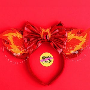 May include: Red Minnie Mouse ears with a large red bow and flame-shaped ears. The ears are decorated with yellow and orange flames. The bow has a rhinestone in the center. The headband is red.