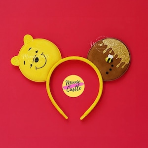 May include: Yellow and brown Minnie Mouse ears with a Winnie the Pooh character on one ear and a honey pot with a bee on the other ear. The headband is yellow.