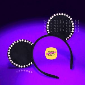 May include: Black mouse ear headband with silver spike studs around the ears. The headband has the text "Minnie Castle" on a yellow square. The background is a gradient of purple and blue.
