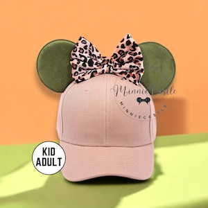 May include: A pink baseball cap with attached green mouse ears and a leopard print bow. The cap has the text "Minnie Castle" printed on the front. The hat is designed for both kids and adults.