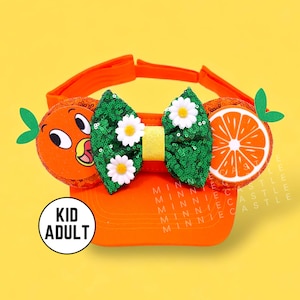 May include: Orange-themed visor with a green sequin bow, white flowers, and an orange slice with a cartoon orange character on the side. The visor has a "Kid Adult" label.