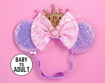 May include: A pink sequined bow headband with a gold crown and Mickey Mouse emblem. The headband has two purple sequined ears and a pink elastic band. The text "BABY TO ADULT" is in a white circle.
