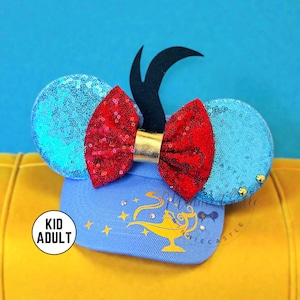 May include: A blue cap with sequined ears and a red sequined bow. The cap features a gold lamp graphic and the text "Kid Adult". The ears are light blue and the bow is red with a gold center.