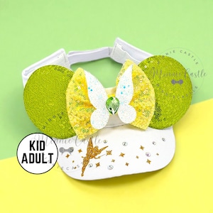 May include: A white headband with a yellow and white bow, green sequined ears, and a white base with a gold fairy graphic. The headband has a "Kid Adult" label.