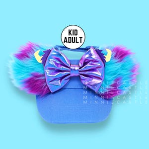 May include: Blue visor with a purple and blue faux fur ear headband and a holographic purple bow. The visor has the text "Kid Adult" on it.