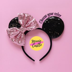 May include: A black headband with sequined mouse ears. One ear is black, the other is pink with a matching sequined bow. The text "Choose your color" is above the ears. The Minnie Castle logo is in the center.