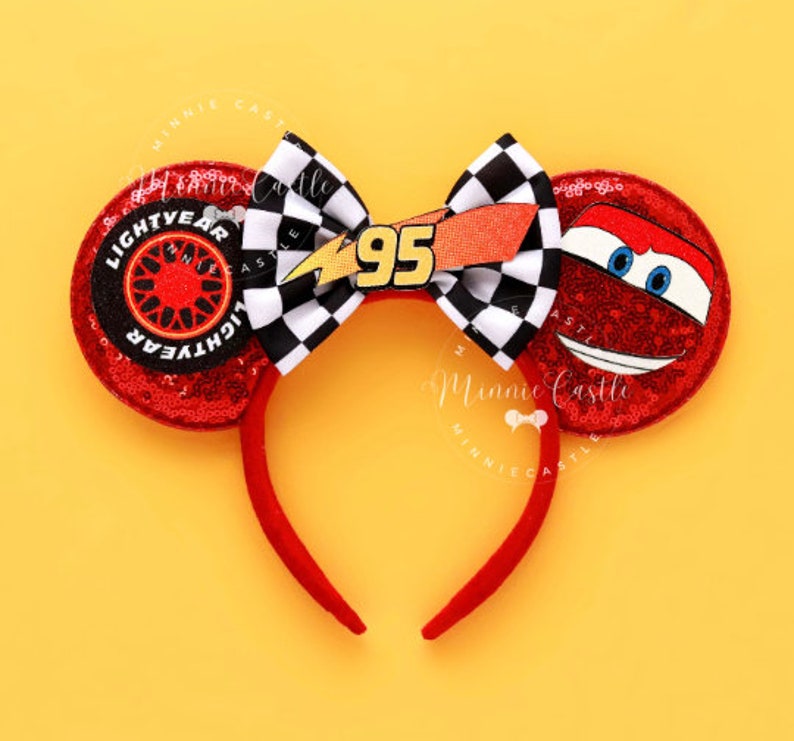 May include: Red sequined mouse ears headband featuring Lightning McQueen and Lightyear designs. The bow has a checkered pattern with the number 95. The headband is red and sits on a yellow background.