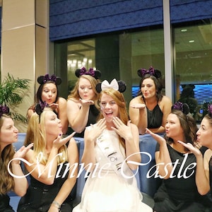 May include: A group of women wearing black dresses and Minnie Mouse ears pose for a photo. The woman in the center is wearing a white dress and a tiara. The text "Minnie Castle" is written in the foreground.