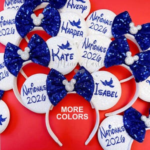 May include: White sequined mouse ear headbands with blue sequin bows and silver Mickey Mouse accents. Some ears have names and "Nationals 2026" printed on them. The image also has the text "MORE COLORS".