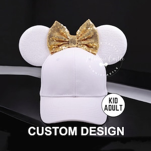 May include: White baseball cap with gold sequin bow and white fuzzy mouse ears. The cap has a black brim and the text "KID ADULT" is on the side. The text "CUSTOM DESIGN" is below the cap.