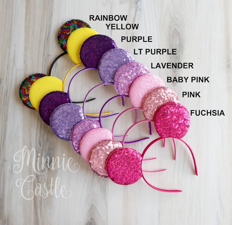 May include: A set of 10 headband ears with different colors of sequins. The colors are rainbow, yellow, purple, light purple, lavender, baby pink, pink, and fuchsia. The headband ears are all on a wooden surface. The text "Minnie Castle" is written on the surface.