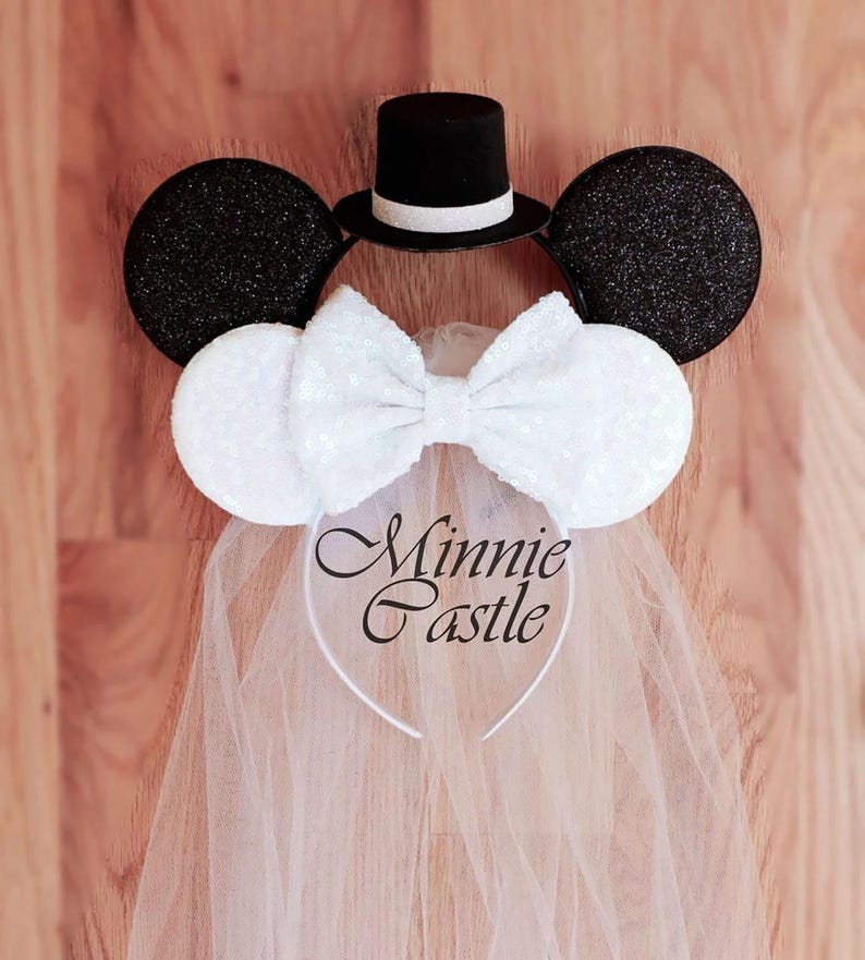 May include: White bridal Minnie Mouse ears with a black top hat, a white bow, and a white tulle veil. The ears are decorated with sequins. The headband says "Minnie Castle".