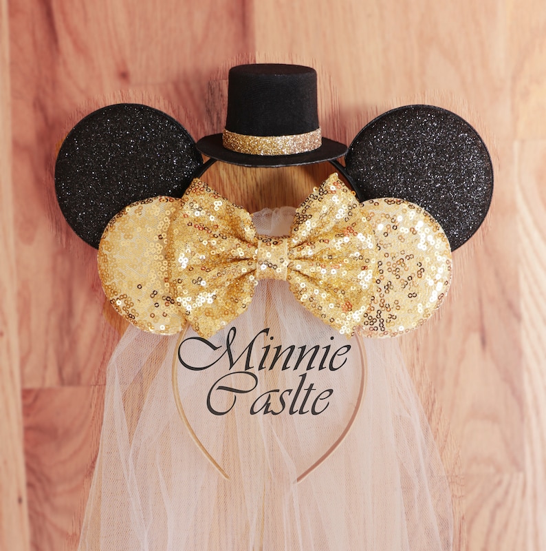 K&ouml;nnte beinhalten: Goldene Pailletten-Minnie-Maus-Ohren mit einem schwarzen Zylinder und einem wei&szlig;en T&uuml;llschleier. Das Stirnband tr&auml;gt die Aufschrift "Minnie Castle".