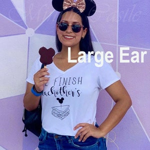 Puede incluir: Una camiseta blanca con un gr&aacute;fico de Mickey Mouse negro y el texto "We finish each other's" impreso en la parte delantera. La persona lleva gafas de sol negras y un par de orejas de Minnie Mouse negras y doradas.