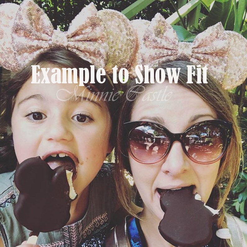 Puede incluir: Dos personas con orejas de Minnie Mouse, una con purpurina rosa y la otra con purpurina dorada, sostienen helados con forma de Mickey Mouse. El texto "Example to Show Fit Minnie Castle" est&aacute; superpuesto a la imagen.