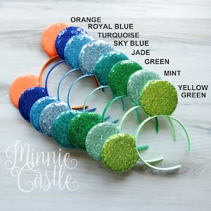 May include: A set of ten Minnie Mouse ears headbands in various shades of green, blue, and orange. The ears are covered in sequins and the headbands are plain.
