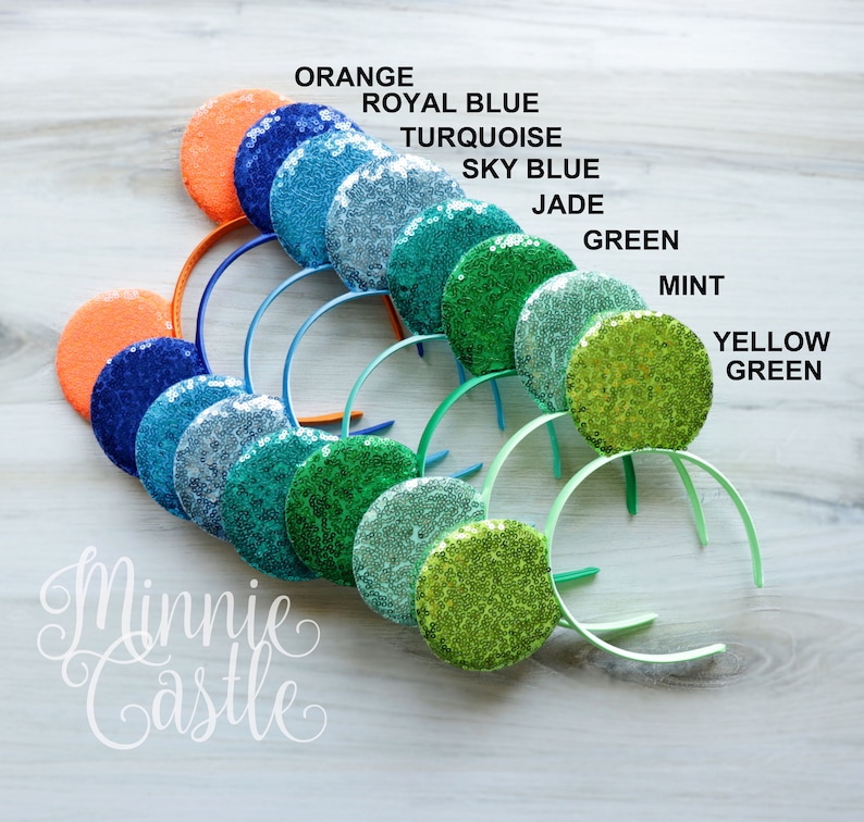 May include: A set of ten Minnie Mouse ears headbands in various shades of green, blue, and orange. The ears are covered in sequins and the headbands are plain.