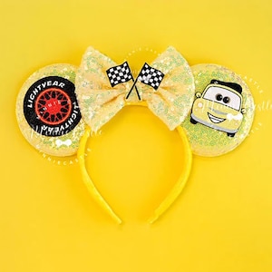 May include: Yellow sequined headband with large ears featuring a bow with two checkered flags. One ear has a tire design with the text "LIGHTYEAR", the other ear has a cartoon car. The headband is a bright yellow color.