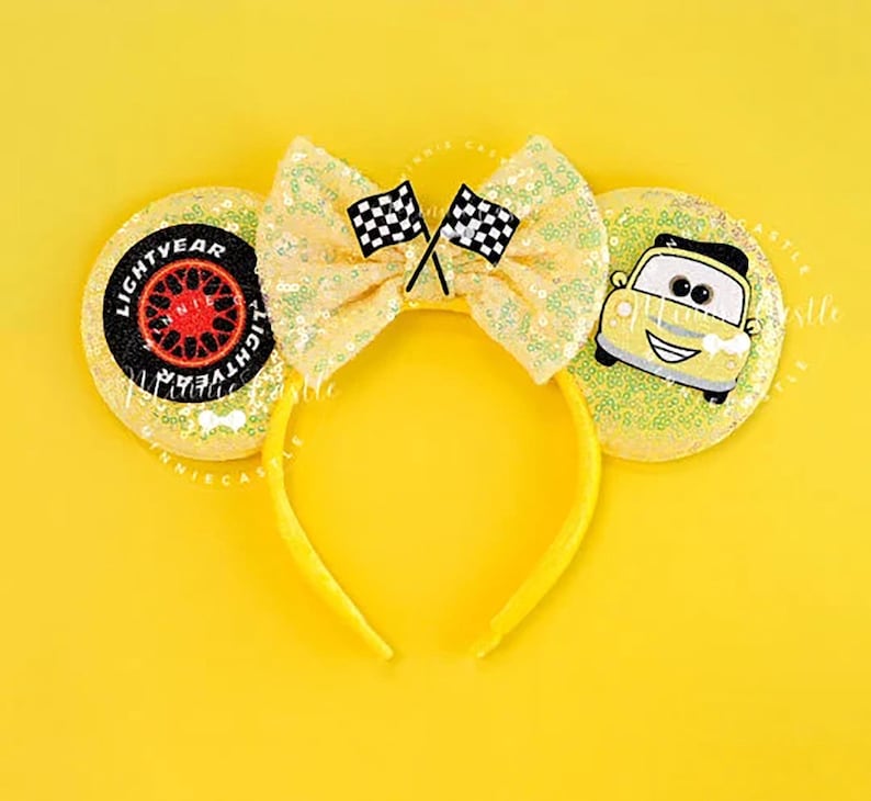 May include: Yellow sequined headband with large ears featuring a bow with two checkered flags. One ear has a tire design with the text "LIGHTYEAR", the other ear has a cartoon car. The headband is a bright yellow color.