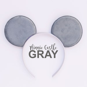 May include: Gray Minnie Mouse ear headband with soft, round ears. The white headband features the text "Minnie Castle GRAY" in black script. The ears are a soft gray color, perfect for a themed outfit.