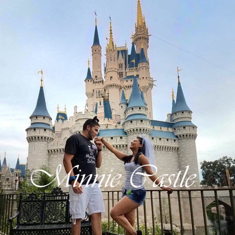 K&ouml;nnte beinhalten: Ein Paar posiert vor dem Schloss von Aschenputtel in Walt Disney World. Die Frau tr&auml;gt einen wei&szlig;en Schleier und ein gestreiftes Hemd. Der Mann tr&auml;gt ein schwarzes T-Shirt mit den Worten "Best Man" und einem wei&szlig;en Mickey-Maus-Kopf. Der Text "Minnie Castle" ist in wei&szlig;en Kursivbuchstaben auf dem Bild geschrieben.