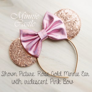 Puede incluir: Orejas de Minnie Mouse de oro rosa con lazo rosa iridiscente. Imagen mostrada: Oreja Minnie de oro rosa con lazo rosa iridiscente