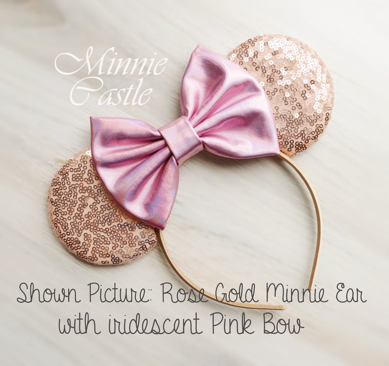 Puede incluir: Orejas de Minnie Mouse de oro rosa con lazo rosa iridiscente. Imagen mostrada: Oreja Minnie de oro rosa con lazo rosa iridiscente