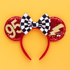 May include: Red sequined mouse ears with a black and white checkered bow. One ear features the number 95 in gold glitter, the other a gold glitter lightning bolt. The headband is red.