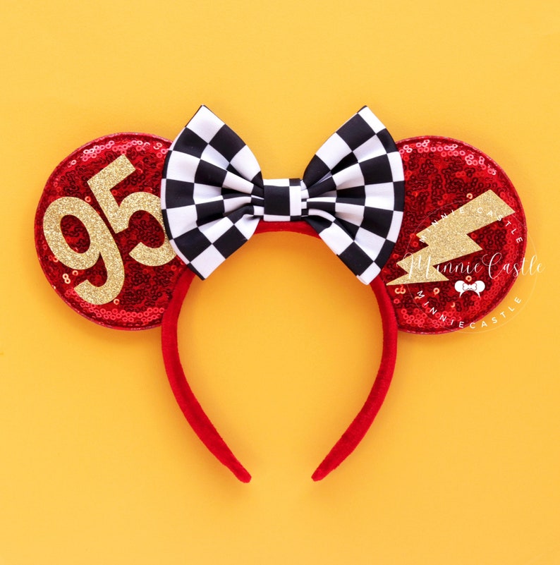 May include: Red sequined mouse ears with a black and white checkered bow. One ear features the number 95 in gold glitter, the other a gold glitter lightning bolt. The headband is red.