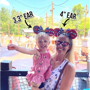 May include: Two women wearing Cars-themed mouse ear headbands. One headband is 3.3 inches, the other is 4 inches. The headbands have red, black, and white accents. The women are smiling in front of a theme park backdrop.