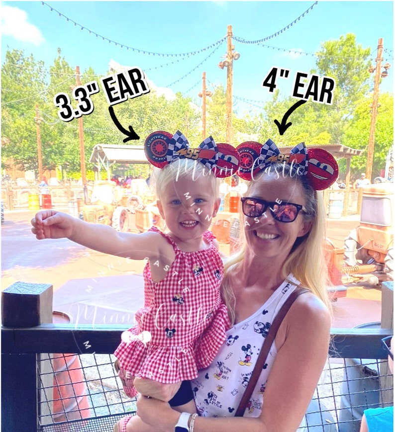 May include: Two women wearing Cars-themed mouse ear headbands. One headband is 3.3 inches, the other is 4 inches. The headbands have red, black, and white accents. The women are smiling in front of a theme park backdrop.