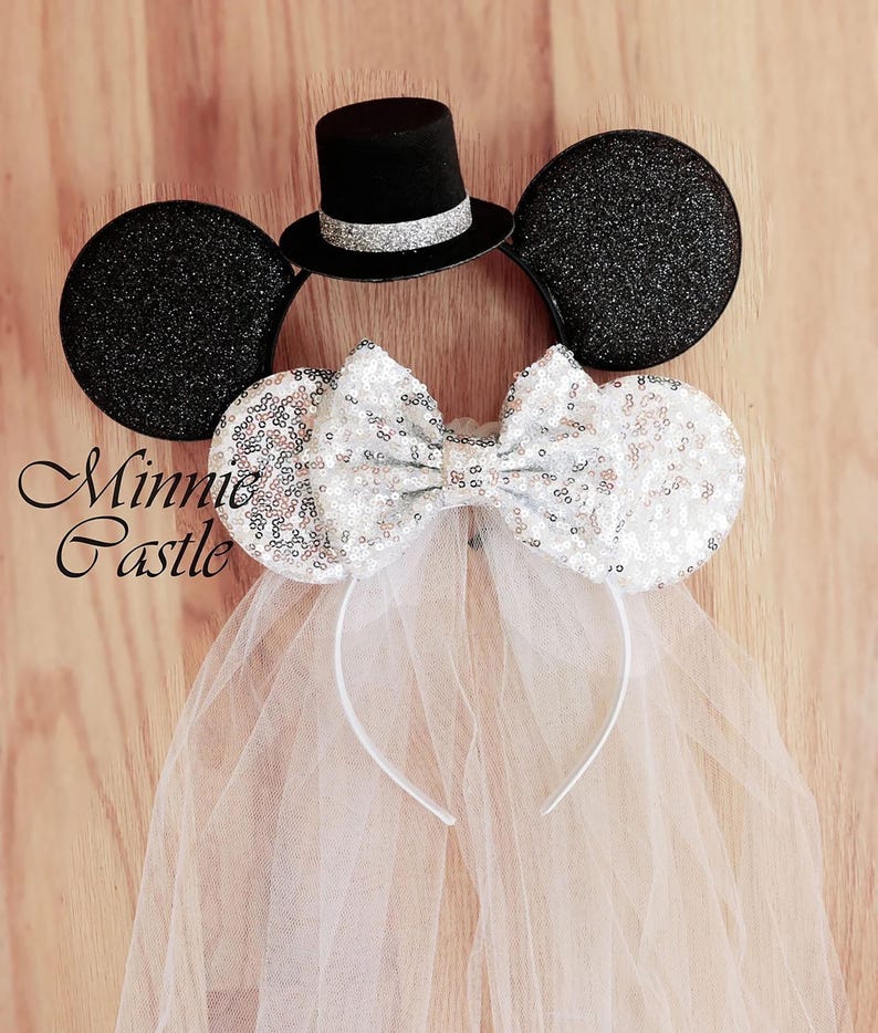 May include: Black Minnie Mouse ears with a white tulle veil and a silver sequined bow. A black top hat with a silver band sits on top of the ears. The text "Minnie Castle" is visible in the image.