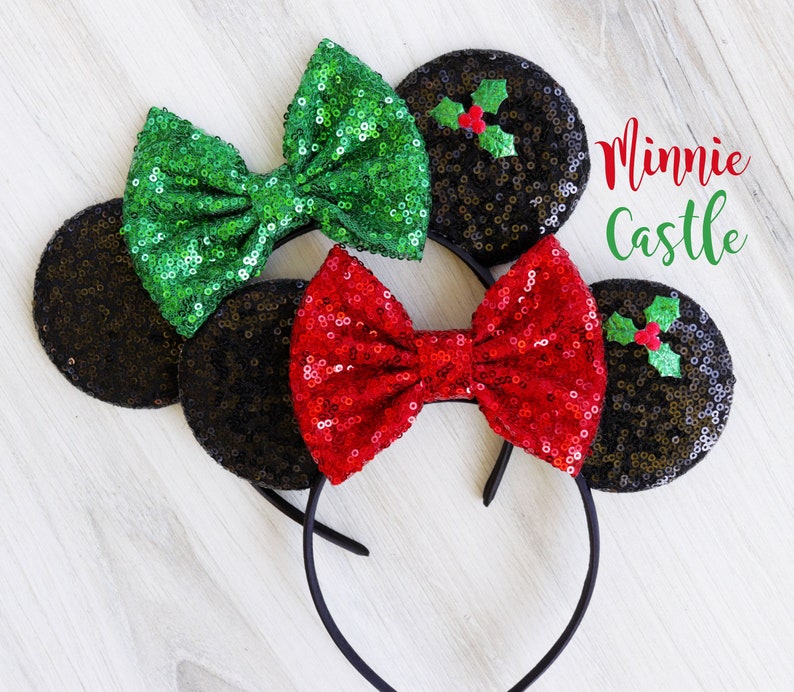 May include: Black sequin Minnie Mouse ears with a red and green bow. The bow has a holly design. The ears have the text "Minnie Castle" on them.