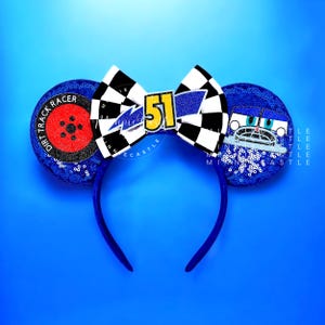 May include: Blue sequined Minnie Mouse ear headband with a racing theme. Features a checkered bow with the number 51, a wheel design, and a car graphic. The ears are blue and the headband is blue.