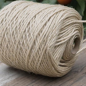 Peut inclure: Une bobine de ficelle naturelle en jute. La ficelle est de couleur beige et est enroulée fermement autour d'un noyau en carton.