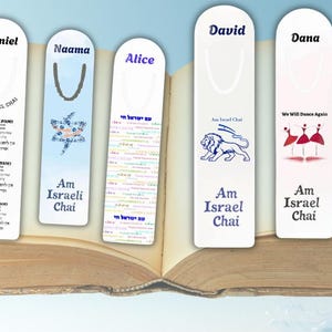 Könnte beinhalten: Fünf weiße Lesezeichen mit Namen und Designs, darunter ein Davidstern, ein Löwe und tanzende Figuren, liegen in einem offenen Buch. Jedes Lesezeichen trägt den Text "Am Israeli Chai" und zusätzlichen Text auf Hebräisch.