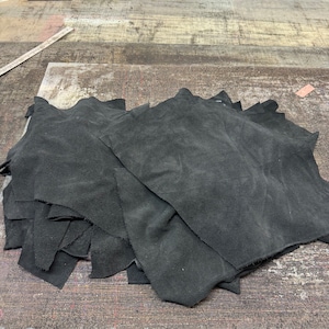 Può includere: Un mucchio di ritagli di pelle scamosciata nera. La pelle è morbida e flessibile, e sarebbe perfetta per progetti di artigianato.